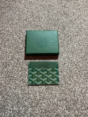 Grön korthållare - Snygg grön korthållare med klassiskt mönster och matchande ask. Tillverkad i läder med vit logotypdetalj. Perfekt för dig som vill ha en stilren och exklusiv accessoar till dina kort.