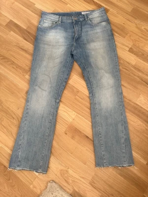 Ljusblå flared jeans med råa kanter - Ljusblå jeans med flared passform och snygga slitningar på benen. Jeansen har råa, fransiga benslut och klassisk femficksdesign. Perfekta för en avslappnad och trendig look. Materialet är denim i bomull.