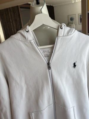 Vit hoodie från Polo Ralph Lauren - Snygg vit hoodie från Polo Ralph Lauren med dragkedja framtill och klassisk logga broderad på bröstet. Säköpt den och tagit av lapparna så kan ej lämna tillbaka som jag ville eftersom den inte passa mig i storlek skriv om ni undrar något. NYPRIS 2200!!