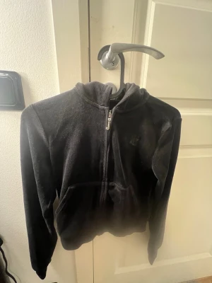 Svart velour hoodie med dragkedja - Säljer en svart hoodie från Juicy Couture i mjuk velour med huva och dragkedja framtill. Tröjan har två fickor och diskret logga på bröstet. Perfekt för dig som gillar en chill och stylish look.