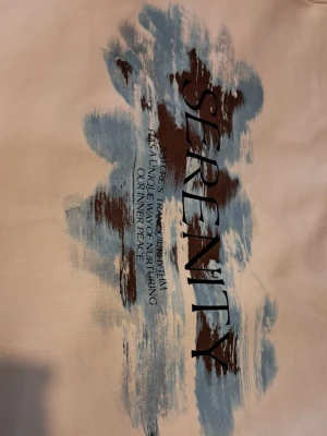 Vit stickad tröja med tryck - Vit stickad tröja från H&M med trycket 'SERENITY' och blåbruna penseldrag på framsidan. Rund halsringning och lång ärm. Perfekt för dig som gillar en chill och stilren vibe. Oversized (M)