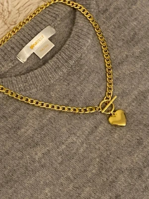 Guldfärgat halsband med hjärthänge - Snyggt guldfärgat rostfritt halsband med en chunky kedja och ett hjärthänge. Halsbandet har en toggle-låsning framtill som ger en trendig touch. Perfekt accessoar för att lyfta din outfit med en cool detalj.