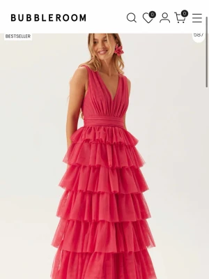 Rosa volangklänning från Bubbleroom - Säljer denna vackra långa rosa/röda klänning från Bubbleroom med djup v-ringning och bred midja. Klänningen har flera lager av volanger som ger ett dramatiskt och elegant intryck. Perfekt för speciella tillfällen och har ärmlös design. Helt ny o skulle använda på balen, men blir tyvärr inte av. Så säljer för 1250kr och ordinarie pris 1800 kr. 