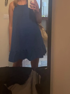 Blå sommarklänning med volang - Snygg blå kort klänning med tunna axelband och volang nertill. Perfekt för varma dagar och enkel att styla med sneakers eller sandaler. Klänningen har en lös passform och är tillverkad i ett lätt material som känns skönt mot huden.