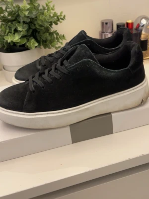 Svarta sneakers med vit sula - Stilrena svarta sneakers med ovandel i mockaliknande material och klassisk vit, tjock sula. Skorna har svarta skosnören och en enkel, clean design som passar till det mesta. Perfekta för dig som gillar en minimalistisk look. Jack and Jones skor.