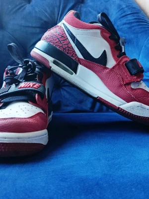 Nike Air Jordan Legacy 312 Low röd/vit - Snygga Nike Air Jordan Legacy 312 Low sneakers i rött, vitt och svart med ikonisk Swoosh och Jumpman-logga. Skorna har läderöverdel, svart rem över snörningen och detaljer i elefantmönster. Perfekta för dig som gillar streetstyle och basketinspirerad design.