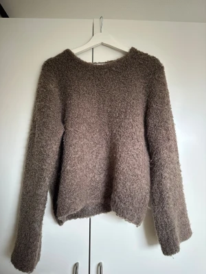 Brun fluffig stickad tröja Lindex - Mysig brun stickad tröja från Lindex med fluffig, lurvig textur. Tröjan har rund halsringning och långa ärmar, perfekt för kyliga dagar. Enkel och stilren design som är lätt att matcha med olika outfits.