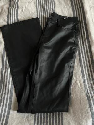 Svarta coated jeans  - Snygga svarta coated jeans från Vero moda. Lågmidjade och utsvängda i benen. Storlek XS. Använda en gång 
