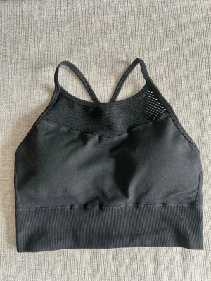 Svart sport-bh från BLACC - Svart sport-bh från BLACC med smala korsade axelband och nät upptill. Bh:n har bred resår nedtill och är tillverkad i ett stretchigt material som passar perfekt för träning eller en aktiv vardag.