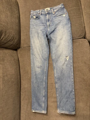 Ljusblå jeans från Paige med slitningar - Säljer ett par ljusblå jeans från Paige med snygga slitningar och raka ben. Jeansen har klassisk femficksdesign, bälteshällor och en skön passform. Perfekta för dig som gillar en avslappnad men trendig stil.