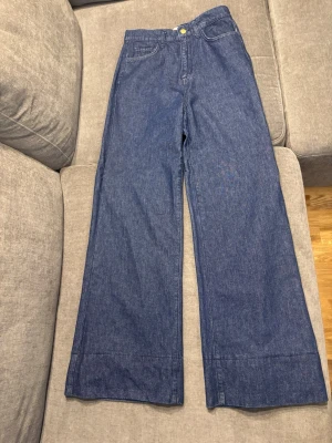 Blåa wide leg jeans från Triarchy - Snygga blå jeans från Triarchy med vid passform och hög midja. Klassisk femficksdesign och knappgylf. Tillverkade i slitstark denim med en avslappnad silhuett som ger en modern och trendig look. Perfekta för både vardag och uppklädda tillfällen.