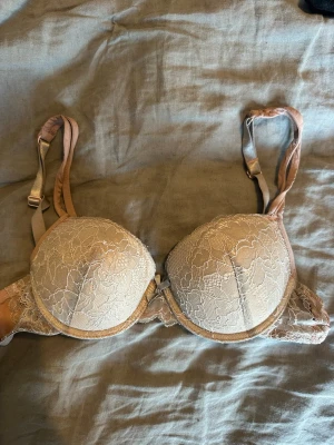 Beige spets-bh med vaddering 70A - Snygg beige bh med vadderade kupor och spetsdetaljer. Justerbara axelband och bygel för extra stöd. Perfekt för dig som gillar en feminin och stilren look. Materialet är mjukt och bekvämt mot huden.