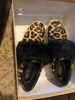 Leopardmönstrade sneakers Michael Kors - Snygga sneakers från Michael Kors med leopardmönster i brunt och svart. Skorna har en fluffig svart detalj över vristen och är tillverkade i hårkalv. Perfekta för dig som vill sticka ut med din stil.
