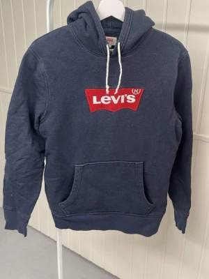 Mörkblå Levi's hoodie med logga - Mörkblå hoodie från Levi's med stor röd och vit broderad logga på bröstet.l.