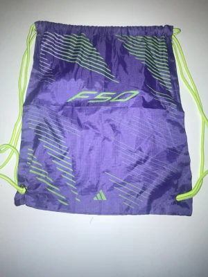 Adidas F50 lila fotbollsskor - Säljer ett par Adidas F50 fotbollsskor i lila med neongula detaljer och snörfri design. Skorna har en lätt ovandel i syntetmaterial och fasta dobbar för spel på gräs. Medföljer matchande gympåse i samma färgtema. Men lite sönder