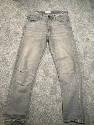 Jack & Jones gråa jeans relaxed Chris - Snygga grå jeans från Jack & Jones med relaxed passform och klassisk femficksdesign. Jeansen har en diskret tvättad look och är tillverkade i denim. Perfekta för en stilren och avslappnad vibe. Storlek: W28 L32