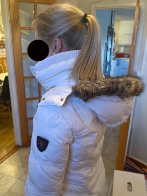 Vit pufferjacka päls + snörning - Snygg vit pufferjacka från Esprit med hög krage, huva med fuskpäls och dekorativa svarta snörningar framtill. Jackan har quiltad design och ett märke på ärmen. Perfekt för kalla dagar när du vill hålla stilen. Höst/Vinter eller kyliga sommarkvällar.