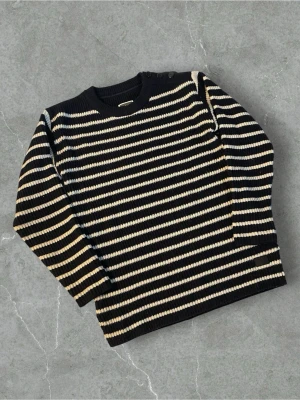 Randig stickad tröja från G-Star RAW | L - Säljer en stickad tröja från G-Star RAW i marinblått med vita och beige horisontella ränder. Tröjan har rund halsringning, ribbstickade muddar och knappdetalj vid axeln. Perfekt för dig som gillar klassisk men cool stil.