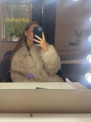 Beige fluffig fuskpäls kappa - Supermjuk och oversized beige fuskpäls kappa med bred krage och lång ärm. Perfekt för att hålla värmen under kalla dagar och ger en lyxig känsla till din outfit. Stängs framtill och har en klassisk, rak passform.