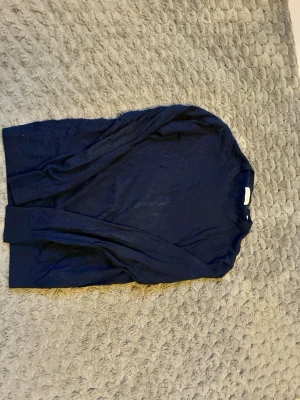 Mörkblå stickad tröja från Jack and Jones  - En enkel och stilren mörkblå stickad tröja med rund hals och långa ärmar. Tröjan har ribbstickade muddar vid ärmslut och nederkant, vilket ger en klassisk look. Perfekt att matcha med jeans eller kjol.