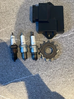 Tändstift, kugghjul och tändbox - Säljer tre tändstift från NGK och BRISK, ett kugghjul i metall samt en svart tändbox. Perfekt för dig som mekar med moppe eller motorcykel och behöver reservdelar. Allt på bilden ingår.