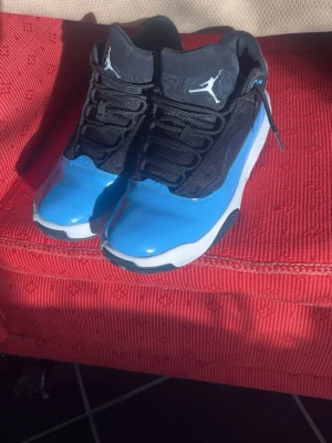 Jordan sneakers blå och svarta - Snygga Jordan sneakers i blått och svart med vit sula och Jumpman-logga på sidan och plösen. Skorna har lågt skaft, svarta skosnören och detaljer i glansigt material framtill. Perfekta för dig som vill sticka ut med en sportig och cool stil.