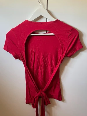 Röd topp med öppen rygg och knyt  - Trendig röd topp med korta ärmar, rund halsringning och en snygg öppen rygg med knytband. Tunn och mjuk bomullskänsla.