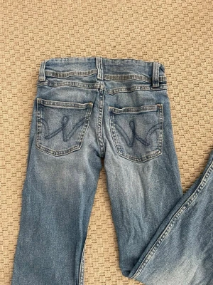 Blå jeans från Gina Tricot - Ett par klassiska blå jeans från Gina Tricot med snyggt slitna detaljer och broderade bakfickor. Jeansen är bootcut och kontrastsömmar som ger en cool look. Perfekta till en avslappnad stil.