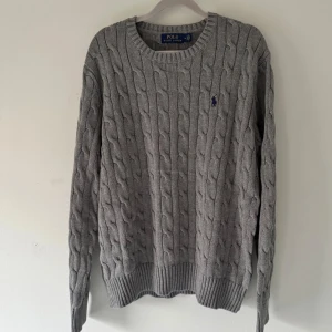 Polo Ralph Lauren kabelstickad tröja - Tjena! Säljer en stilren grå kabelstickad tröja från Polo Ralph Lauren. Färgen är grå. Mycket bra skick, inga tecken på användning. Passar formella eller avslappnade outfits. Säljer för endast 499kr, köpt från Zalando för 2395kr. Inga skambud. Hör av er vid funderingar 🙌. 