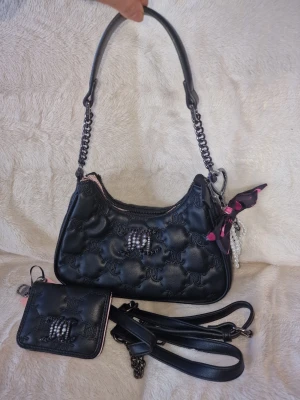 Svart Juicy Couture handväska med plånbok - Snygg svart handväska från Juicy Couture med quiltat mönster och pärlbroderad logga. Väskan har kedjedetaljer, avtagbar axelrem och en liten scarf i rosa och svart. Matchande plånbok i svart och ljusrosa med logga och kortfack ingår.