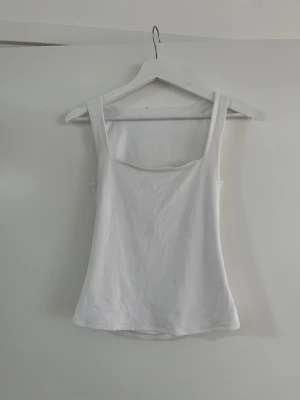 Vit ärmlös linnetopp - En enkel och stilren vit linnetopp med breda axelband och rak halsringning. Toppen är ärmlös och har en klassisk passform som passar till många olika stilar. Perfekt att matcha med jeans eller kjol.