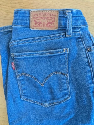 Levi's 714 Straight blå jeans - Blå klassiska jeans från Levi's, modell 714 Straight. W26 L32 Jeansen har raka ben, fem fickor och ikonisk läderpatch bak. Materialet är slitstark denim med snygga kontrastsömmar och röd Levi's-tag på bakfickan. Perfekt för en avslappnad och cool look.