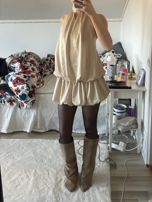 Beige kort klänning med öppen rygg - Säljer en beige kort klänning med halterneck, öppen rygg och inbyggda shorts. En riktig fest klänning. Jag är 167.