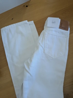Vita straight jeans från Denim - Säljer ett par helt nya vita jeans med straight fit och låg midja. Jeansen har klassiska fem fickor, silverfärgade nitar och en snygg Monki-läderpatch bak. Perfekta för dig som gillar en clean och enkel look.