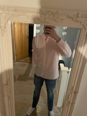 Ljusrosa skjorta från Gant - Säljer en stilren ljusrosa skjorta från Gant, modell University Oxford Regular Fit. Skjortan har klassisk krage, långa ärmar och knäppning framtill. Perfekt för dig som gillar en clean och enkel look.