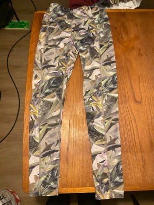 Mönstrade leggings från SOC - Säljer ett par snygga leggings från SOC med tropiskt bladmönster i grönt, gult och lila toner. Tillverkade i tekniskt funktionsmaterial med bra andningsförmåga. Perfekta för träning eller chill dagar.