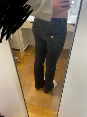 Jättesnygga svarta bootcut jeans med fickdetaljer - Säljer ett par jättesnygga svarta bootcut jeans med snygga fickor bak som har lock och knappdetalj. Jeansen har låg midja och klassisk femficksdesign. Perfekta för dig som gillar en avslappnad men ändå trendig look. Säljer då de nt kommer till användnig längre ❤️
