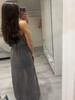 Svartvit axelbandslös maxiklänning - Snygg axelbandslös långklänning i svartvitt mönster med slits på sidan. Klänningen har ett elastiskt band upptill och ett diskret bladmönster. Perfekt för varma dagar och enkel att styla med accessoarer. Passar även en S skulle jag säga 