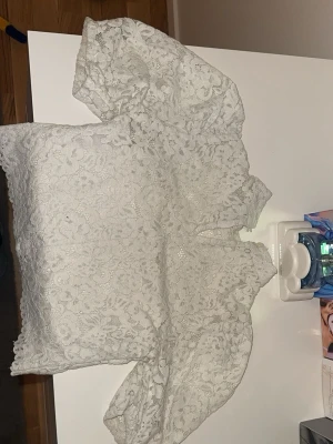 Vit spetsblus med puffärm - Superfin vit blus i spets med blommigt mönster och puffiga korta ärmar. Perfekt för dig som vill ha en romantisk och trendig look. Blusen har hög hals och är genombruten i materialet vilket ger en luftig känsla.