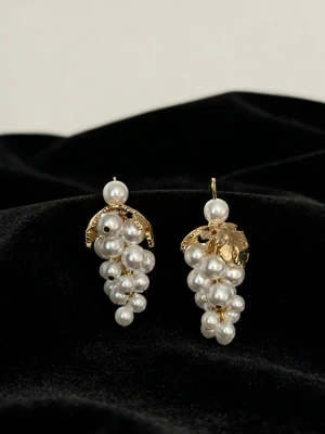 Guldörhängen med pärlklasar - Unika örhängen i form av vindruvsklasar med vita pärlor och guldfärgade detaljer. Örhängena har en elegant design med flera små pärlor som hänger i klasar och ett dekorativt blad i metall upptill. Perfekta för dig som vill sticka ut med accessoarer som känns lyxiga och trendiga.