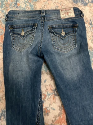 Blå True Religion bootcut - Säljer ett par blå jeans från True Religion med snygga kontrastsömmar och dekorativa ficklock bak. Säljer på grund av för stora❤️🩷 helt oandvända 