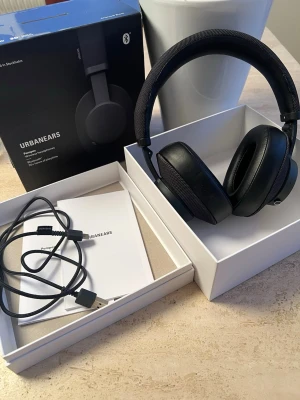 Svarta Urbanears Bluetooth-hörlurar - Stilrena svarta over-ear hörlurar från Urbanears med mjuka öronkuddar i konstläder och tygklädd bygel. Trådlös Bluetooth-anslutning och medföljande laddkabel. Perfekta för musik, gaming eller poddar. Snygg minimalistisk design och bekväm passform.