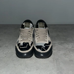 Valentino rockrunners - Snygga sneakers från Valentino med beige mockadetaljer och svart, grå och vit camo-mönstrad textil. Skorna har robust svart sula och klassisk låg siluett. Perfekta för dig som vill sticka ut med exklusiv streetstyle. hör av dig vid minsta intresse🤩🤩.