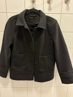 Svart ullkappa från Wera - Stilren svart ullkappa från Åhléns  med klassisk krage och stora framfickor. Kappan har rak passform, knäppning med stora knappar och helfoder. Perfekt för dig som gillar minimalistisk och tidlös design. Jag är 155 för referens hur den sitter på.