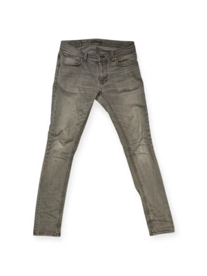 Grå skinny jeans från Nudie Jeans - Snygga grå skinny jeans från Nudie Jeans med klassisk femficksmodell och diskreta slitningar. Jeansen har en smal passform och är tillverkade i stretchigt denimtyg för extra komfort. Perfekta för en trendig och avslappnad stil.