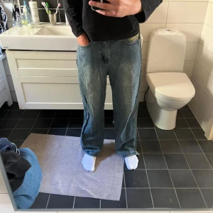 Ed Hardy jeans med drakbroderi - Säljer ett par blå jeans från Ed Hardy med fett broderad drake i blått, gult och svart längs ena benet. Baktill finns en stor gul Ed Hardy-logga. Modellen är loose fit med raka ben och klassisk femficksdesign. Perfekt för dig som vill sticka ut med coola detaljer. Notera ett hål vid backfickan se sista bilden 