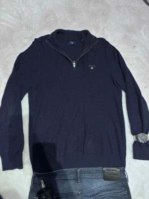 Mörkblå halvzip tröja från Gant - Snygg mörkblå tröja från Gant med halv dragkedja och diskret logga på bröstet. Tröjan har ribbade muddar vid ärmslut och nederkant samt en klassisk ståkrage. Perfekt för lager på lager och passar till jeans eller chinos.