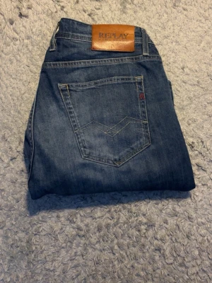 Blå jeans från Replay - Snygga blå jeans från Replay med klassisk femficksdesign och knäppning med knappar. Jeansen har en cool tvättad look och detaljerade sömmar på bakfickan. Perfekta för dig som gillar en avslappnad men trendig stil.