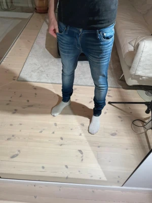 Blå slim fit jeans från Jack & Jones  - Säljer ett par blå slim fit jeans från Jack & Jones  med snygg tvätt och stretchigt material. Jeansen har klassiska fem fickor, låg midja och smala ben. Perfekta för dig som gillar en modern och tajt look.