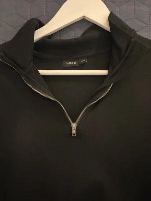 Svart halfzip hoodie från LMTD - Stilren svart hoodie från LMTD med halv dragkedja framtill och hög krage. Tillverkad i mjukt material och har långa ärmar. Stilig och passar till allt.